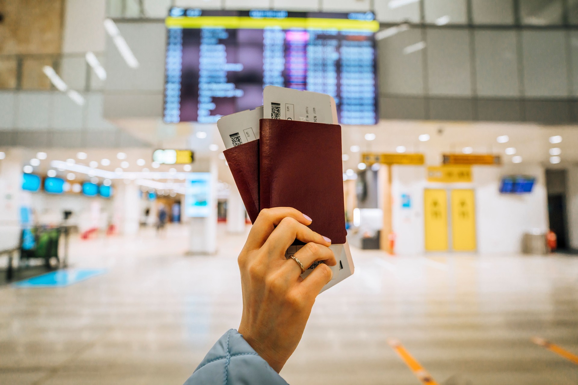 Woman holding passports in front of a flight information board